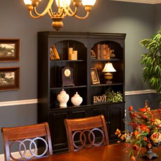 A well-decorated dining room with a wooden table, elegant chairs, and a black bookshelf adorned with decor items.