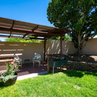 A sunny backyard with a pergola and outdoor seating on a well-kept lawn.