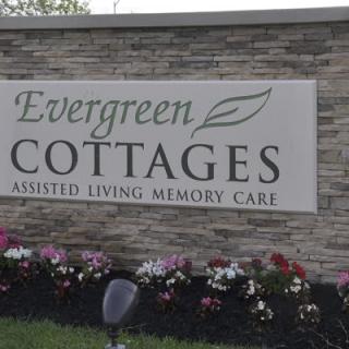 Sign for Evergreen Cottages Assisted Living and Memory Care with surrounding flowers.