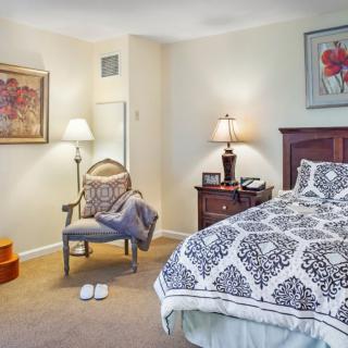 A cozy bedroom with patterned bedding, a chair, and decorative lamps.