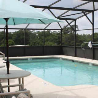 An outdoor pool with a screened enclosure and patio furniture, including an umbrella.