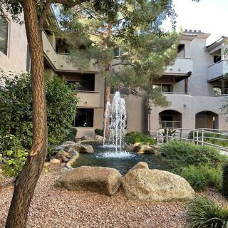 A serene apartment courtyard with a central fountain surrounded by trees and rocks.