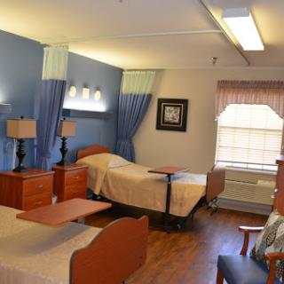 A well-lit hospital room featuring two beds, wooden furniture, and a cozy atmosphere.