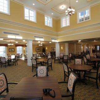 A spacious and elegantly designed dining area featuring multiple tables and chairs, with chandeliers hanging from the high ceiling.
