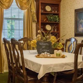 A cozy dining room with a table set for a meal, adorned with a flower centerpiece and surrounded by wooden chairs.