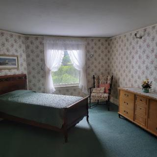 A cozy, vintage-styled bedroom featuring a bed, dresser, and a chair by the window.