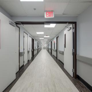 A wide view of a hospital hallway with multiple doors and bright lighting.