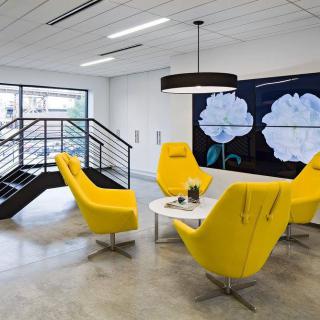 A modern office meeting area featuring bright yellow chairs and minimalist decor.