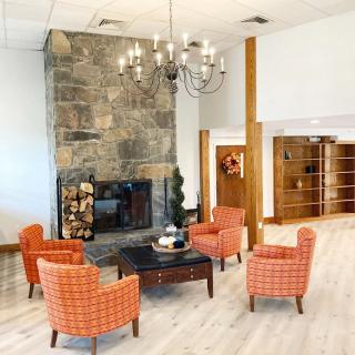 A modern lounge area with a stone fireplace, surrounded by orange chairs and a chandelier overhead.
