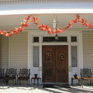 A welcoming porch decorated with autumn-themed garlands above the entrance, featuring several chairs lined up for outdoor seating.