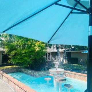 A tranquil outdoor scene with a blue umbrella shading a small fountain and pool.