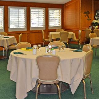A well-arranged dining room with round tables and chairs, featuring white tablecloths and large windows.