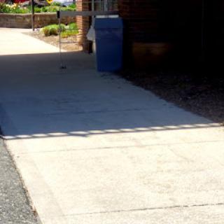 A clear view of a sidewalk beside a building with a blue trash can.