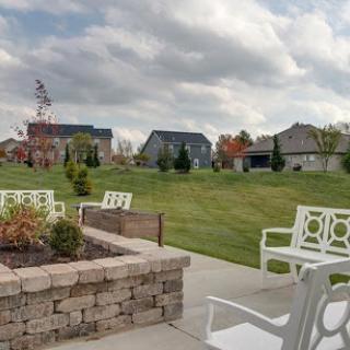A serene outdoor patio area with seating, overlooking a lush green landscape and residential homes under a cloudy sky.