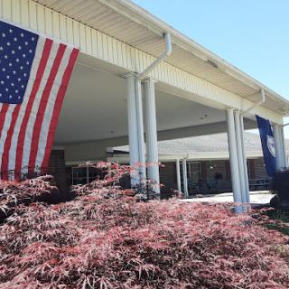 A view of a building adorned with American and state flags, surrounded by colorful foliage.