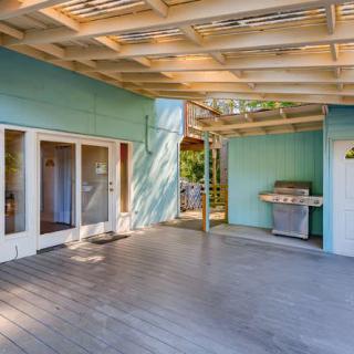 A cozy outdoor patio area featuring a deck, grill, and blue walls under a pergola.