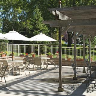 A sunny outdoor patio with tables, chairs, and umbrellas in a garden setting.