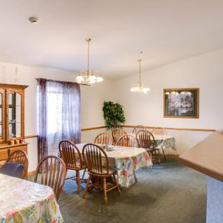 A cozy dining room setup with wooden tables and chairs, decorated with soft lighting and a touch of greenery.