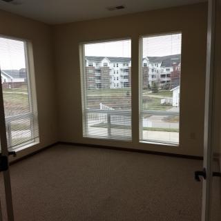 An empty bedroom in an apartment with large windows letting in natural light.