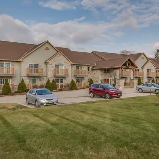 A residential apartment complex with cars parked in front, surrounded by a well-maintained lawn under a cloudy sky.