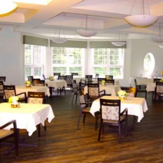 A spacious dining room with neatly arranged tables and chairs, featuring large windows and elegant lighting.