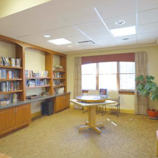 A cozy reading room featuring bookshelves, a round table, and natural light from the windows.
