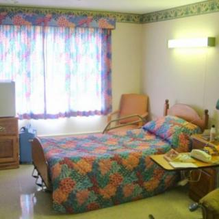 A hospital room with a single bed, patterned bedding, and a window with colorful curtains.