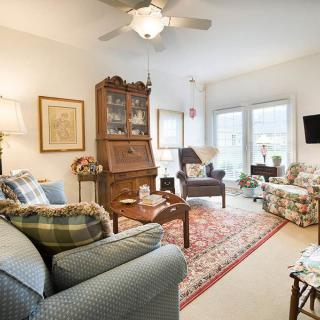 A cozy living room with traditional decor, featuring comfortable seating, a bookshelf, and abundant natural light.