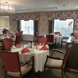 An elegant dining room with tables set for a meal, featuring a chandelier and large windows.