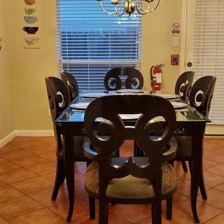 A cozy dining room with a glass-top table and six ornate chairs under a chandelier.