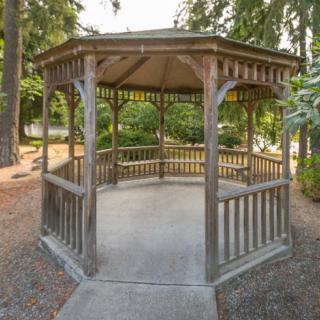A wooden gazebo in a park setting surrounded by trees.