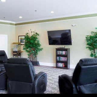Comfortable lounge area with recliner chairs facing a TV and bookshelf, adorned with decorative plants.