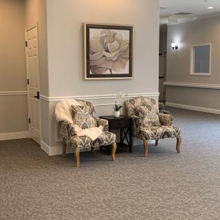 A cozy waiting area with two floral-patterned chairs and a small table, complemented by a painting on the wall.