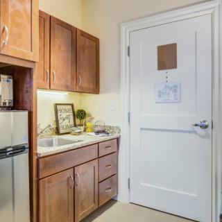 A small kitchen area with wooden cabinets, a sink, and a refrigerator next to a door.
