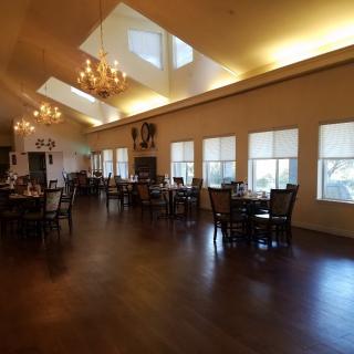 An elegant dining hall with wooden floors and chandeliers, featuring neatly arranged tables and chairs.