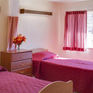 A cozy bedroom with two single beds, pink bedding, and a window with matching curtains.