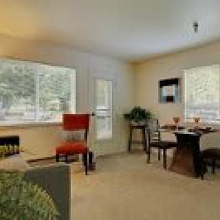 A cozy living room with a dining area, featuring a table and chairs near large windows.