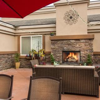 An inviting outdoor patio with a stone fireplace and wicker furniture, accented by potted plants under a red umbrella.
