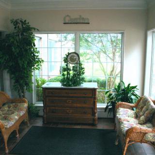 A cozy living room with wicker furniture, decorative plants, and a large window.