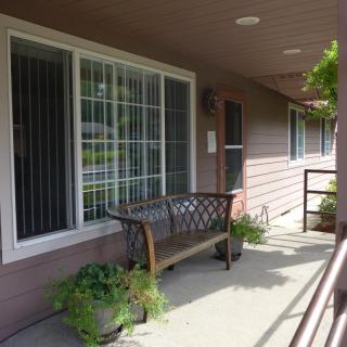 A porch area with a bench and potted plants next to a house window.