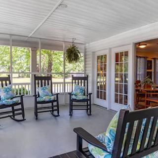 A cozy screened porch featuring several black rocking chairs and a view into the home through French doors.