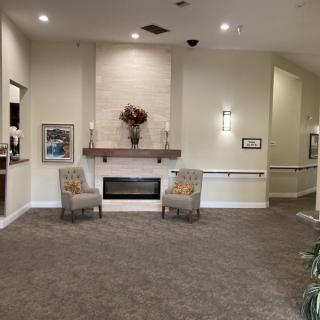 A cozy lobby area featuring a fireplace with two chairs and subtle decor.