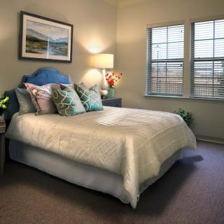 A cozy bedroom with a well-decorated bed, soft lighting, and natural light coming through the window.
