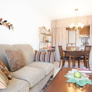 A bright living and dining area with a comfortable sofa, decorative cushions, and a wooden coffee table.