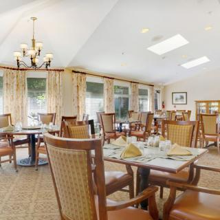 A well-lit dining room with neatly arranged tables and chairs, featuring large windows and a chandelier.