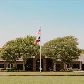 A serene view of a building accompanied by the American and Texas flags, surrounded by lush greenery.