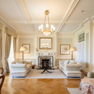 Elegant living room with traditional decor, featuring white sofas, a chandelier, and a central fireplace.