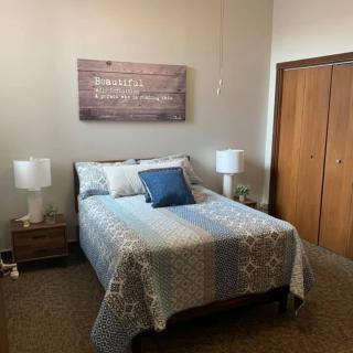 A cozy bedroom with a neatly made bed, two side lamps, and a wooden closet.