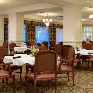 An elegant dining room with well-arranged tables and chairs, featuring classic decor and ambient lighting.