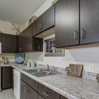 A modern kitchen with dark cabinets, a marble-like countertop, and stainless steel sink.